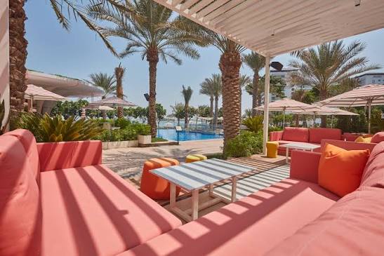 Foto panorâmica de um luxuoso beach club em Dubai ao pôr do sol, com piscina de borda infinita voltada para o mar cristalino e o skyline moderno da cidade ao fundo. Espreguiçadeiras elegantes, palmeiras iluminadas e atmosfera sofisticada transmitem exclusividade, turismo de luxo e experiência premium nos Emirados Árabes Unidos.