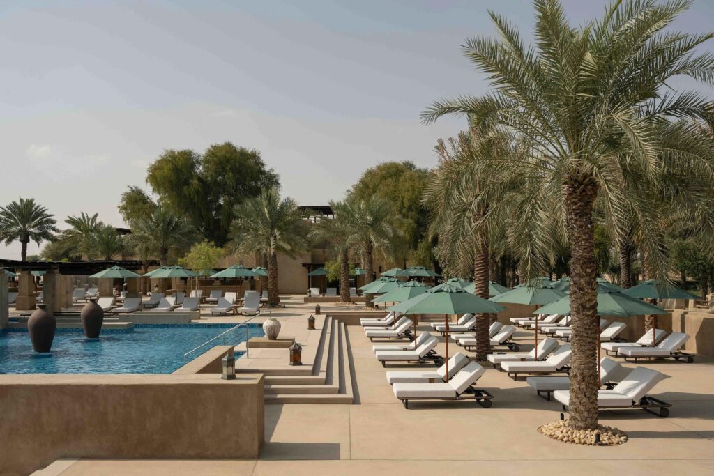 Foto panorâmica de um luxuoso beach club em Dubai ao pôr do sol, com piscina de borda infinita voltada para o mar cristalino e o skyline moderno da cidade ao fundo. Espreguiçadeiras elegantes, palmeiras iluminadas e atmosfera sofisticada transmitem exclusividade, turismo de luxo e experiência premium nos Emirados Árabes Unidos.