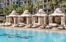 Foto panorâmica de um luxuoso beach club em Dubai ao pôr do sol, com piscina de borda infinita voltada para o mar cristalino e o skyline moderno da cidade ao fundo. Espreguiçadeiras elegantes, palmeiras iluminadas e atmosfera sofisticada transmitem exclusividade, turismo de luxo e experiência premium nos Emirados Árabes Unidos.
