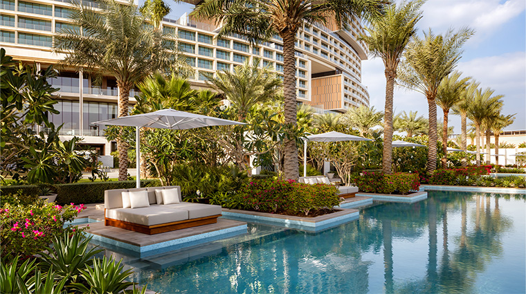 Foto panorâmica de um luxuoso beach club em Dubai ao pôr do sol, com piscina de borda infinita voltada para o mar cristalino e o skyline moderno da cidade ao fundo. Espreguiçadeiras elegantes, palmeiras iluminadas e atmosfera sofisticada transmitem exclusividade, turismo de luxo e experiência premium nos Emirados Árabes Unidos.