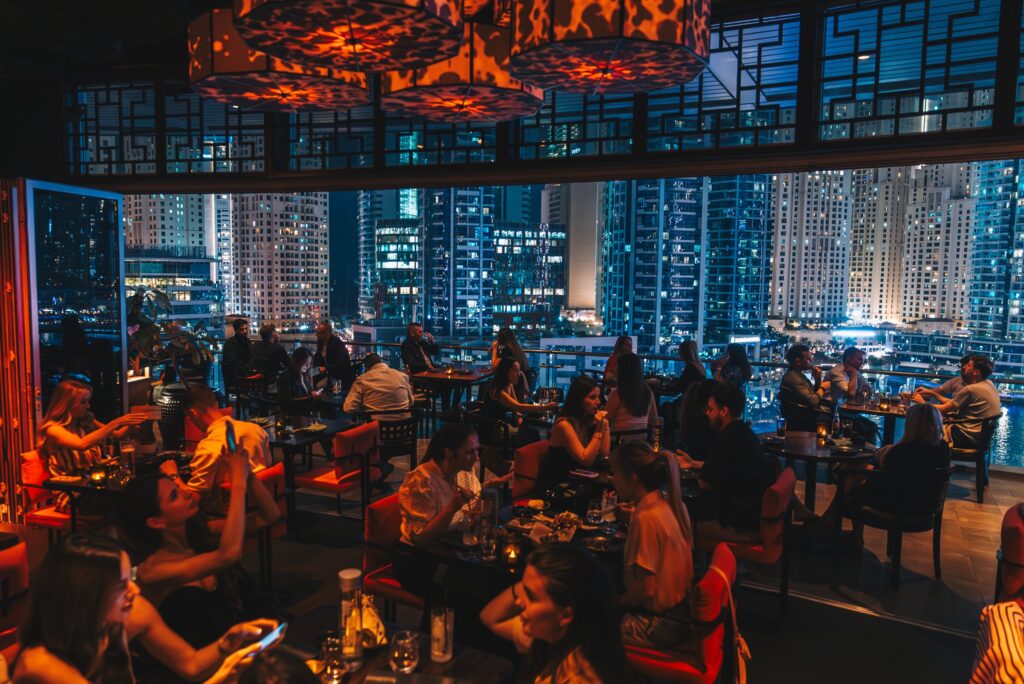 Foto panorâmica de um restaurante luxuoso em Dubai, com vista para o skyline moderno da cidade ao fundo. Ambiente sofisticado com mesas elegantes, decoração refinada e atmosfera exclusiva que transmite uma experiência gastronômica premium e turismo de luxo nos Emirados Árabes Unidos.