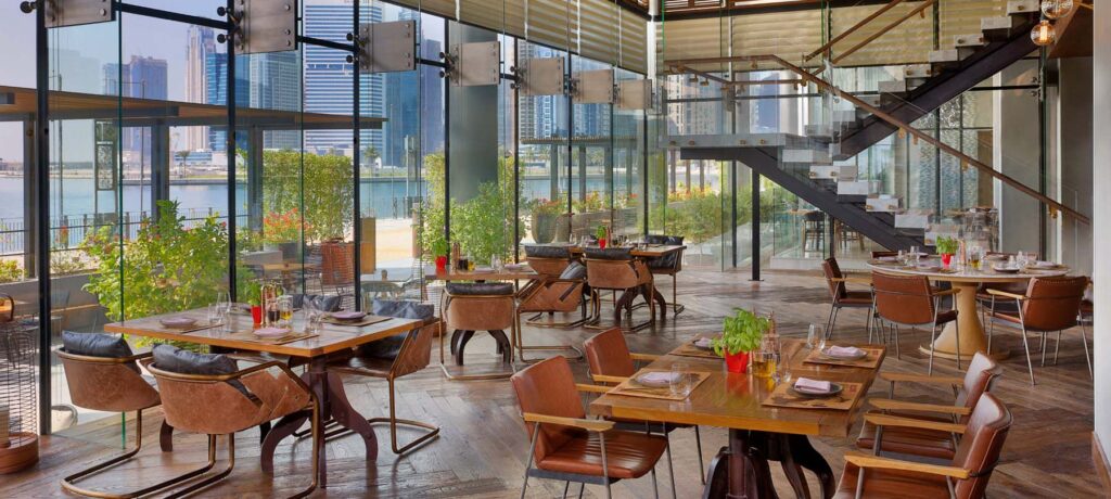 Foto panorâmica de um restaurante luxuoso em Dubai, com vista para o skyline moderno da cidade ao fundo. Ambiente sofisticado com mesas elegantes, decoração refinada e atmosfera exclusiva que transmite uma experiência gastronômica premium e turismo de luxo nos Emirados Árabes Unidos.