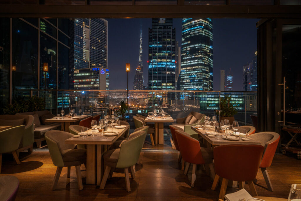 Foto panorâmica de um restaurante italiano luxuoso em Dubai, com salão elegante, mesas brancas impecavelmente montadas, iluminação suave, serviço refinado e ambiente exclusivo no coração financeiro da cidade. Atmosfera clássica, sofisticada e premium, ideal para turismo de luxo, jantares especiais e encontros de negócios nos Emirados Árabes Unidos.