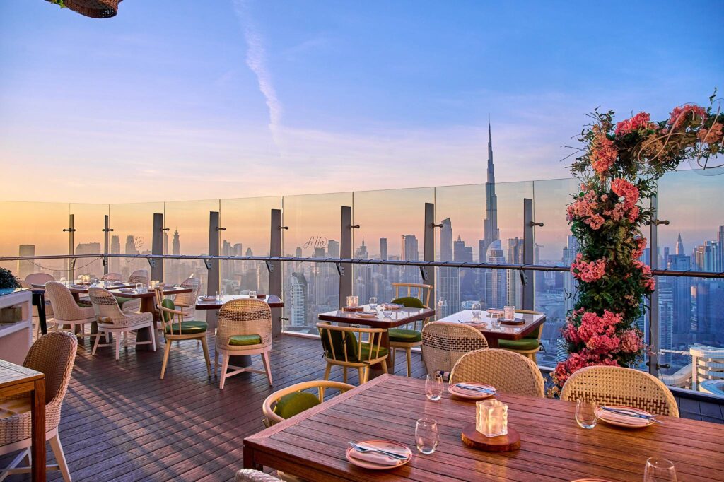Foto panorâmica de um restaurante luxuoso em Dubai, com vista para o skyline moderno da cidade ao fundo. Ambiente sofisticado com mesas elegantes, decoração refinada e atmosfera exclusiva que transmite uma experiência gastronômica premium e turismo de luxo nos Emirados Árabes Unidos.