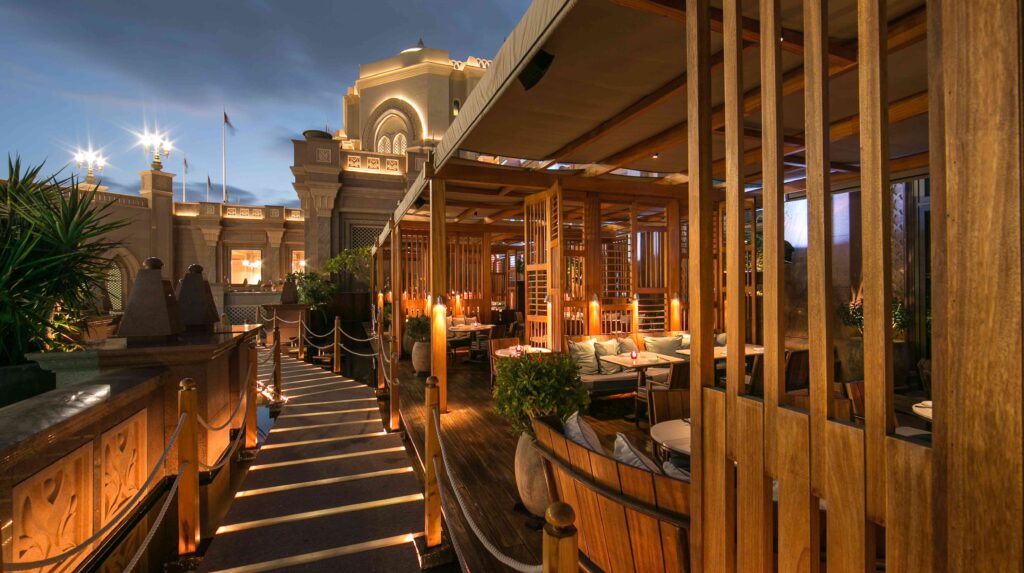 Foto panorâmica de um restaurante italiano luxuoso em Dubai, com salão elegante, mesas brancas impecavelmente montadas, iluminação suave, serviço refinado e ambiente exclusivo no coração financeiro da cidade. Atmosfera clássica, sofisticada e premium, ideal para turismo de luxo, jantares especiais e encontros de negócios nos Emirados Árabes Unidos.
