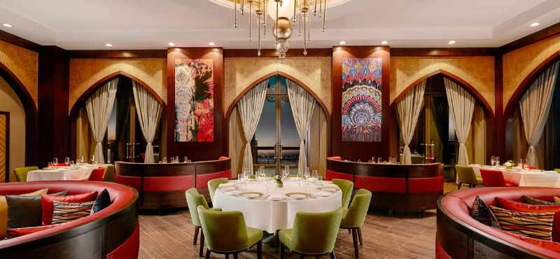 Foto panorâmica de um restaurante italiano luxuoso em Dubai, com salão elegante, mesas brancas impecavelmente montadas, iluminação suave, serviço refinado e ambiente exclusivo no coração financeiro da cidade. Atmosfera clássica, sofisticada e premium, ideal para turismo de luxo, jantares especiais e encontros de negócios nos Emirados Árabes Unidos.