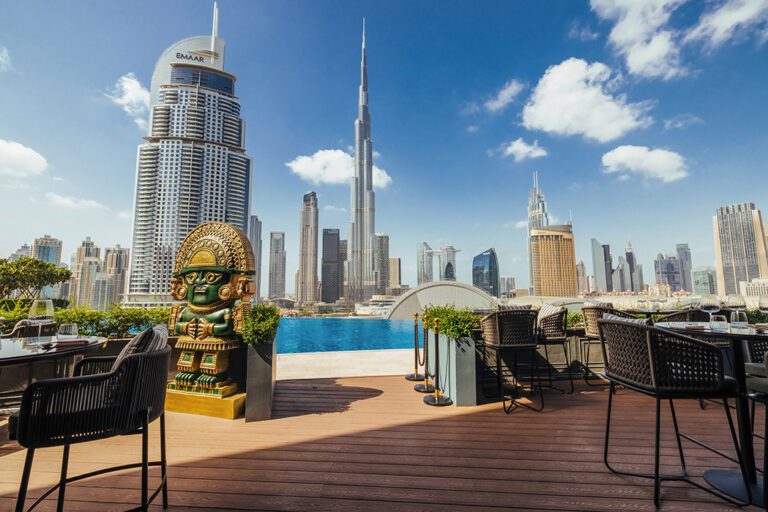 Foto panorâmica de um restaurante luxuoso em Dubai, com vista para o skyline moderno da cidade ao fundo. Ambiente sofisticado com mesas elegantes, decoração refinada e atmosfera exclusiva que transmite uma experiência gastronômica premium e turismo de luxo nos Emirados Árabes Unidos.