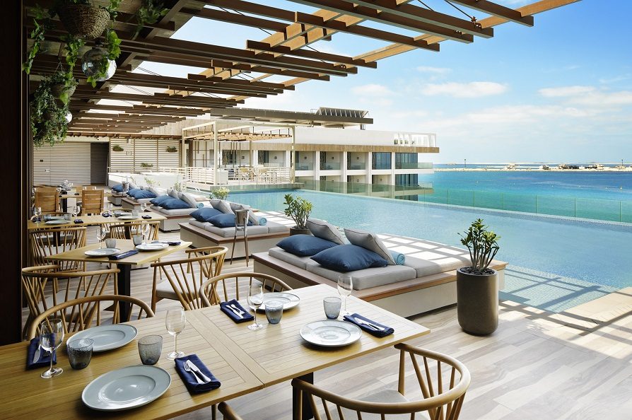 Foto panorâmica de um restaurante luxuoso em Dubai, com vista para o skyline moderno da cidade ao fundo. Ambiente sofisticado com mesas elegantes, decoração refinada e atmosfera exclusiva que transmite uma experiência gastronômica premium e turismo de luxo nos Emirados Árabes Unidos.