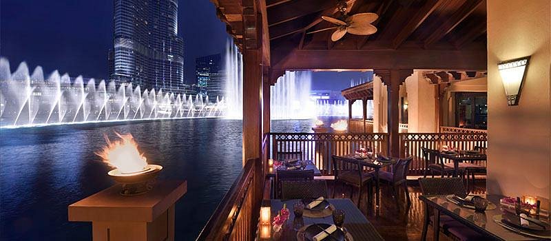 Foto panorâmica de um restaurante luxuoso em Dubai, com vista para o skyline moderno da cidade ao fundo. Ambiente sofisticado com mesas elegantes, decoração refinada e atmosfera exclusiva que transmite uma experiência gastronômica premium e turismo de luxo nos Emirados Árabes Unidos.