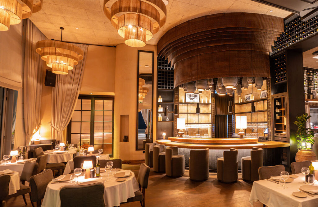 Foto panorâmica de um restaurante italiano luxuoso em Dubai, com salão elegante, mesas brancas impecavelmente montadas, iluminação suave, serviço refinado e ambiente exclusivo no coração financeiro da cidade. Atmosfera clássica, sofisticada e premium, ideal para turismo de luxo, jantares especiais e encontros de negócios nos Emirados Árabes Unidos.