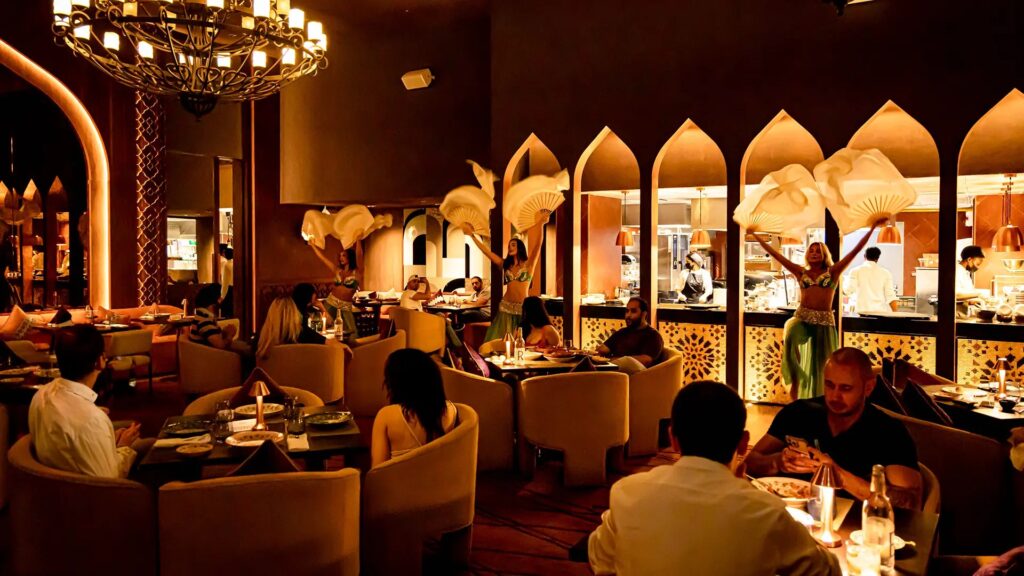 Foto panorâmica de um restaurante italiano luxuoso em Dubai, com salão elegante, mesas brancas impecavelmente montadas, iluminação suave, serviço refinado e ambiente exclusivo no coração financeiro da cidade. Atmosfera clássica, sofisticada e premium, ideal para turismo de luxo, jantares especiais e encontros de negócios nos Emirados Árabes Unidos.