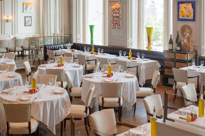 Foto panorâmica de um restaurante grego de luxo em Dubai, com decoração sofisticada em tons claros, frutos do mar frescos expostos, mesas elegantes e ambiente refinado no DIFC. Atmosfera exclusiva que transmite gastronomia mediterrânea premium, luxo e sofisticação internacional.