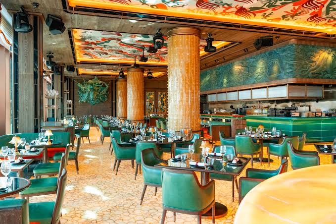Foto panorâmica de um restaurante luxuoso em Dubai, com vista para o skyline moderno da cidade ao fundo. Ambiente sofisticado com mesas elegantes, decoração refinada e atmosfera exclusiva que transmite uma experiência gastronômica premium e turismo de luxo nos Emirados Árabes Unidos.