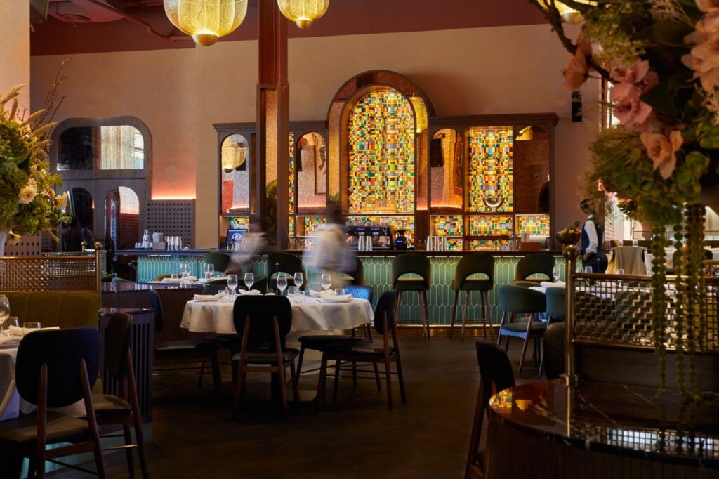 Foto panorâmica de restaurante italiano elegante em Dubai, com frutos do mar frescos, mesas sofisticadas, vista para o Burj Khalifa e para o espetáculo das águas de Dubai ao fundo. Ambiente luxuoso e romântico.